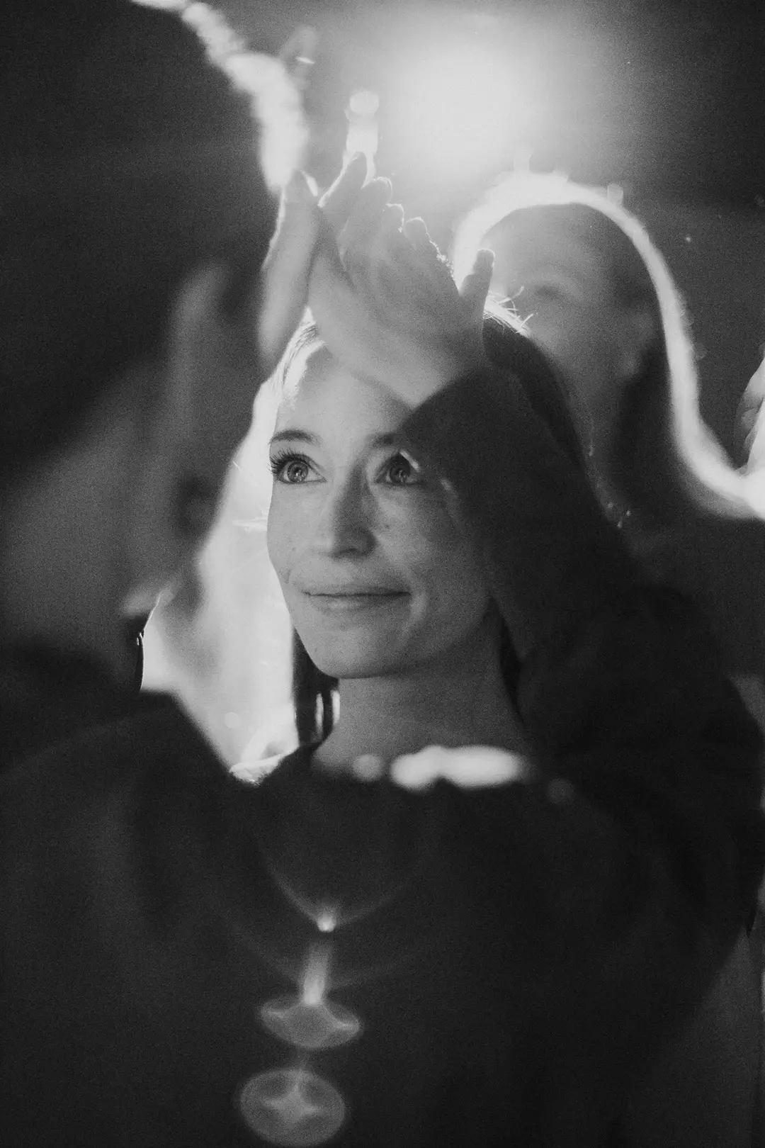 Woman in a crowd gazing upward past clapping hands in hazy light, black and white