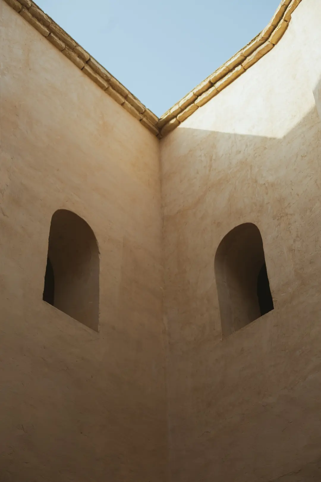 Sand-coloured courtyard walls with two arched niches beneath a pale blue sky