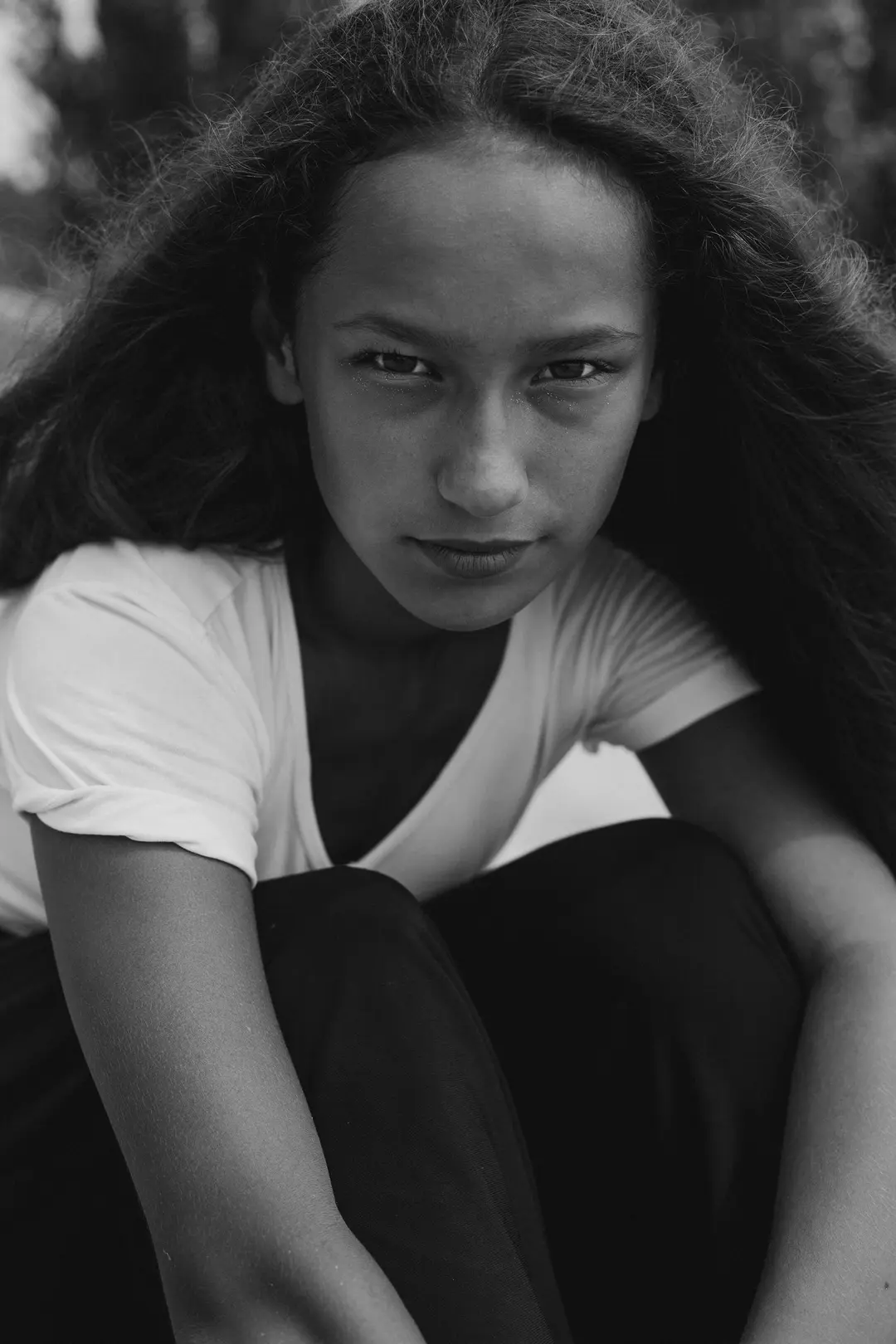 Black and white portrait of a crouching girl with long curls and a direct gaze