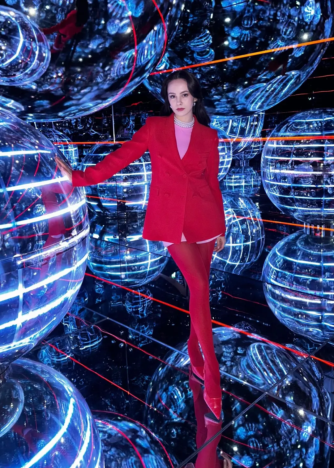 Diana Solonikidi, founder of Disolo Art, in a red suit among glowing mirrored spheres