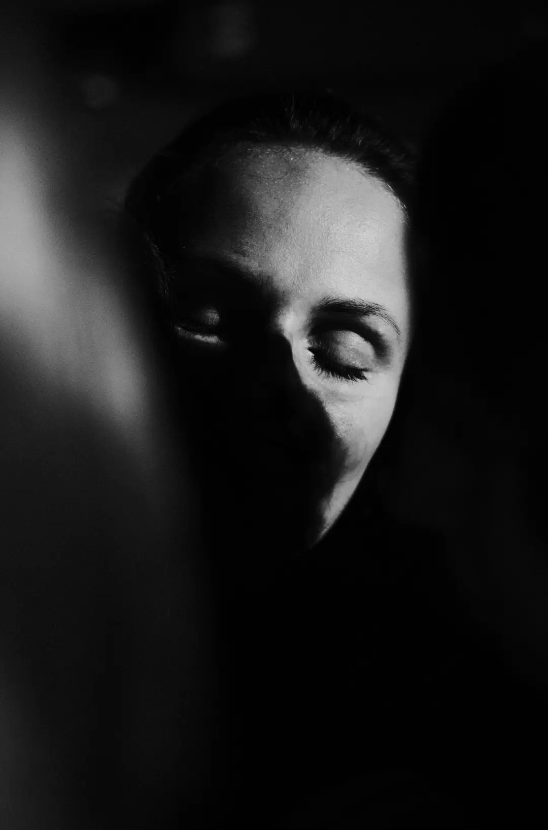 Black and white close-up of a face caught in a narrow slit of light, eyes closed