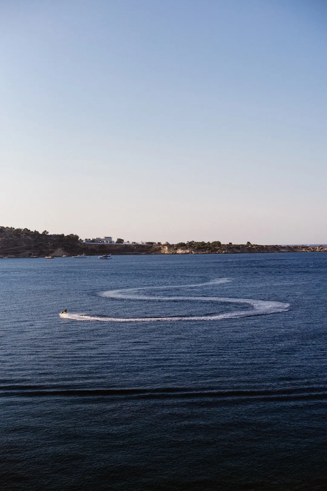 Jet ski carving an S-shaped wake across a deep blue sea beneath a vast dusk sky