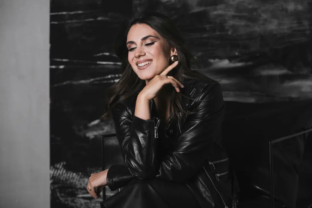 Smiling woman with eyes closed in a black leather jacket, hand raised to her chin