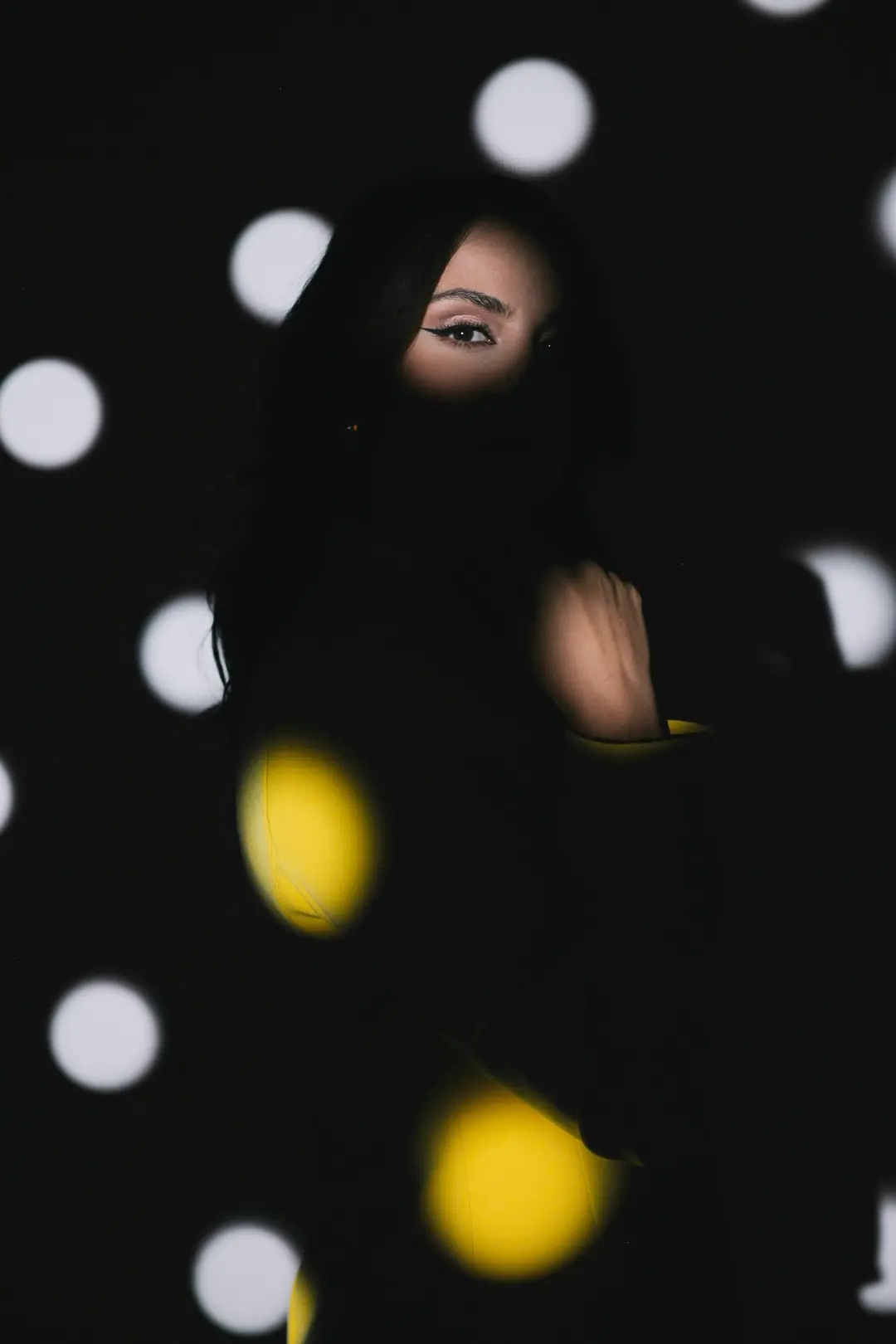 Woman in shadow with only her eye lit, white and yellow polka-dot light projected around her