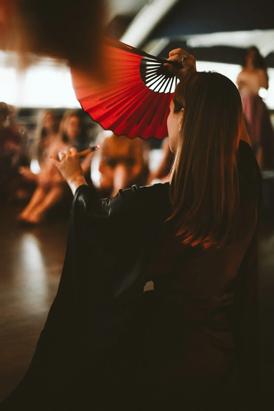Performer in a black satin kimono raising a red fan before a seated audience