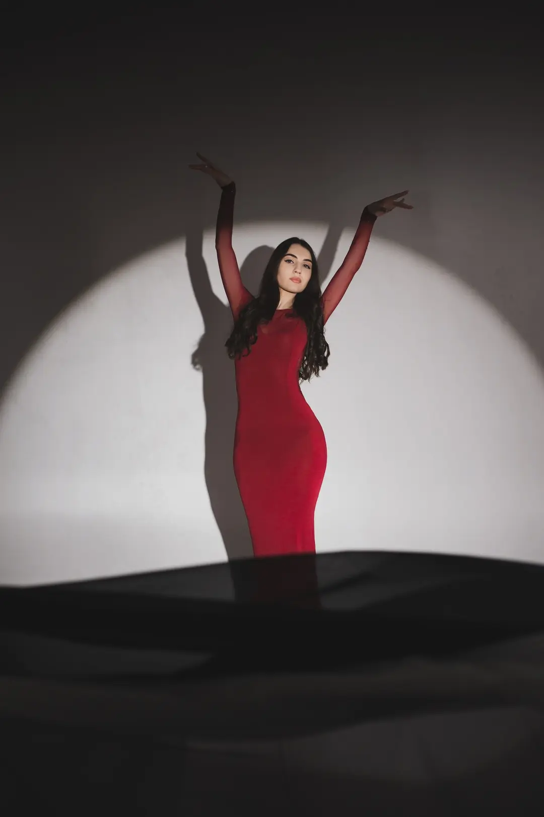 Woman in a red gown raising her arms within a spotlight circle on a grey wall