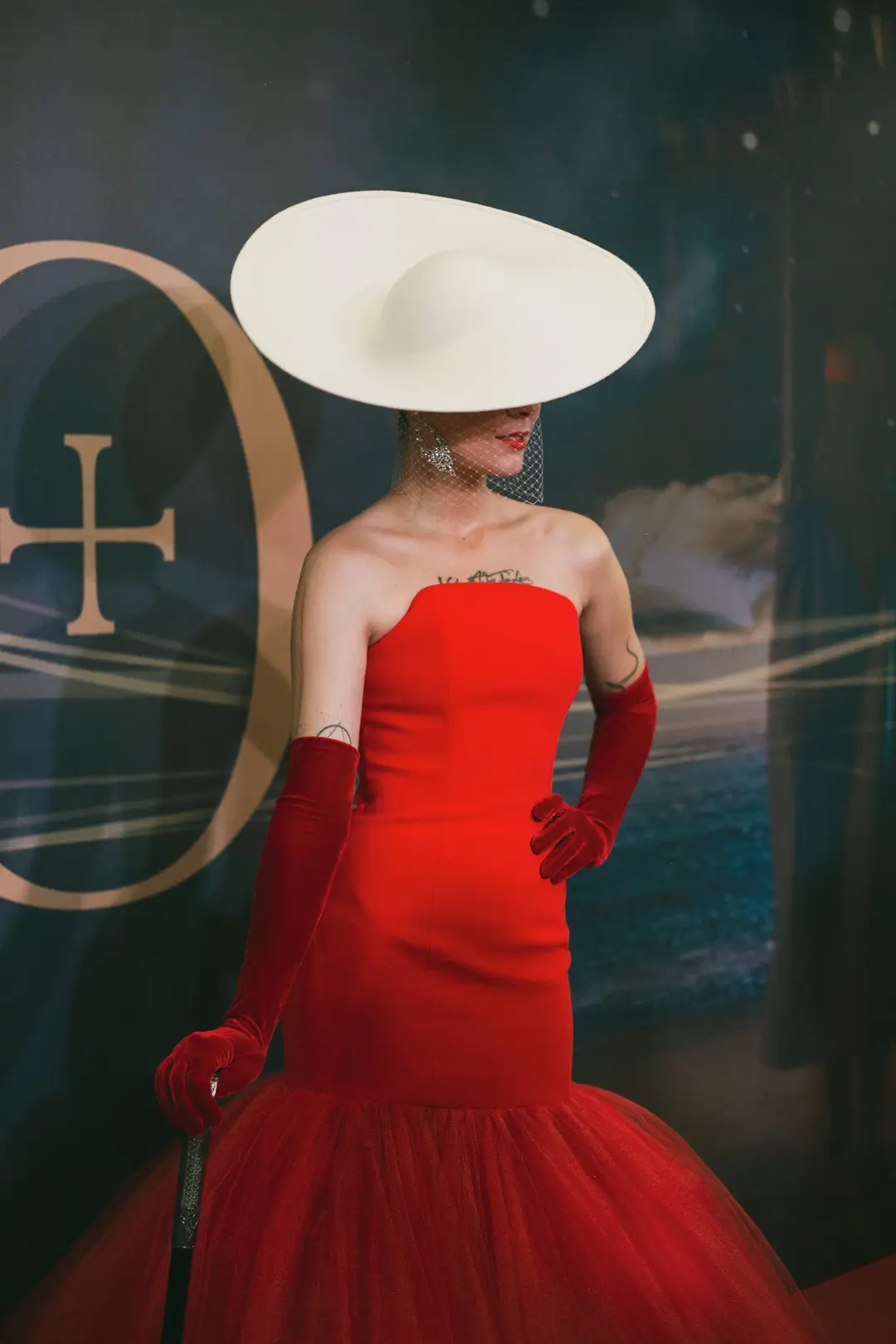 Woman in a strapless red gown and long gloves, face hidden beneath a wide white hat