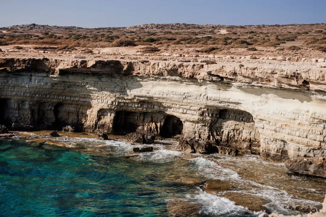 Pale layered sea cliffs hollowed by caves above turquoise surf under a clear sky