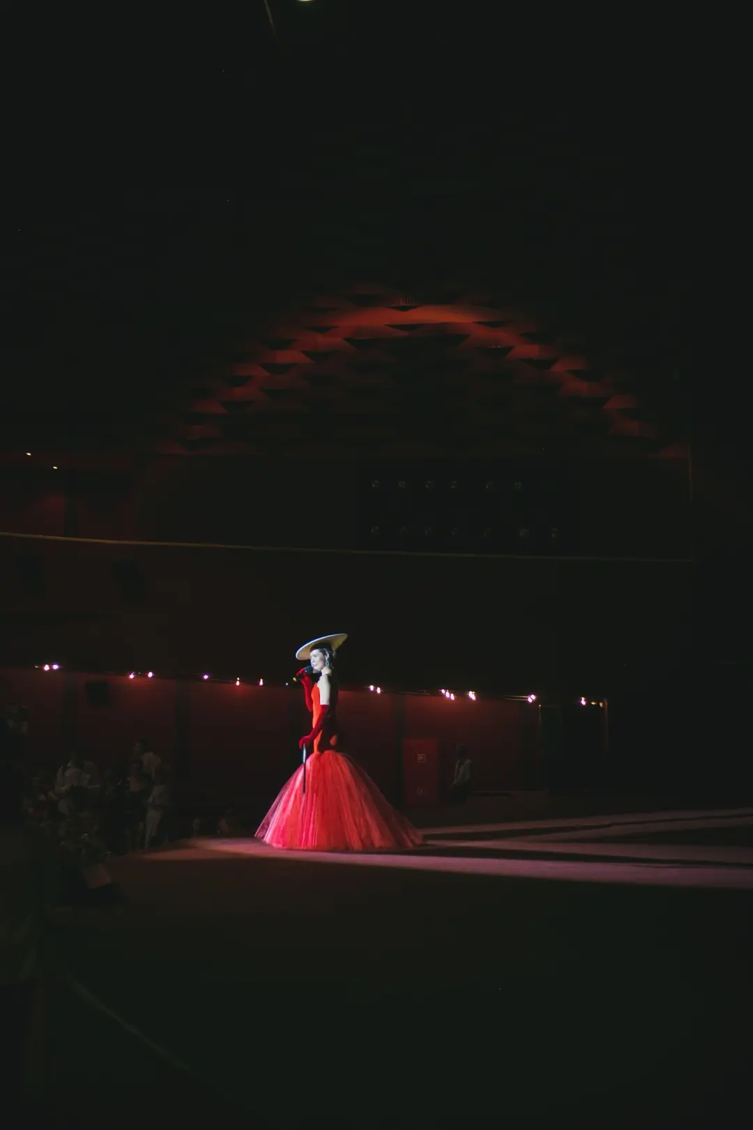 Dark theatre with a singer in a red gown standing in a pool of stage light