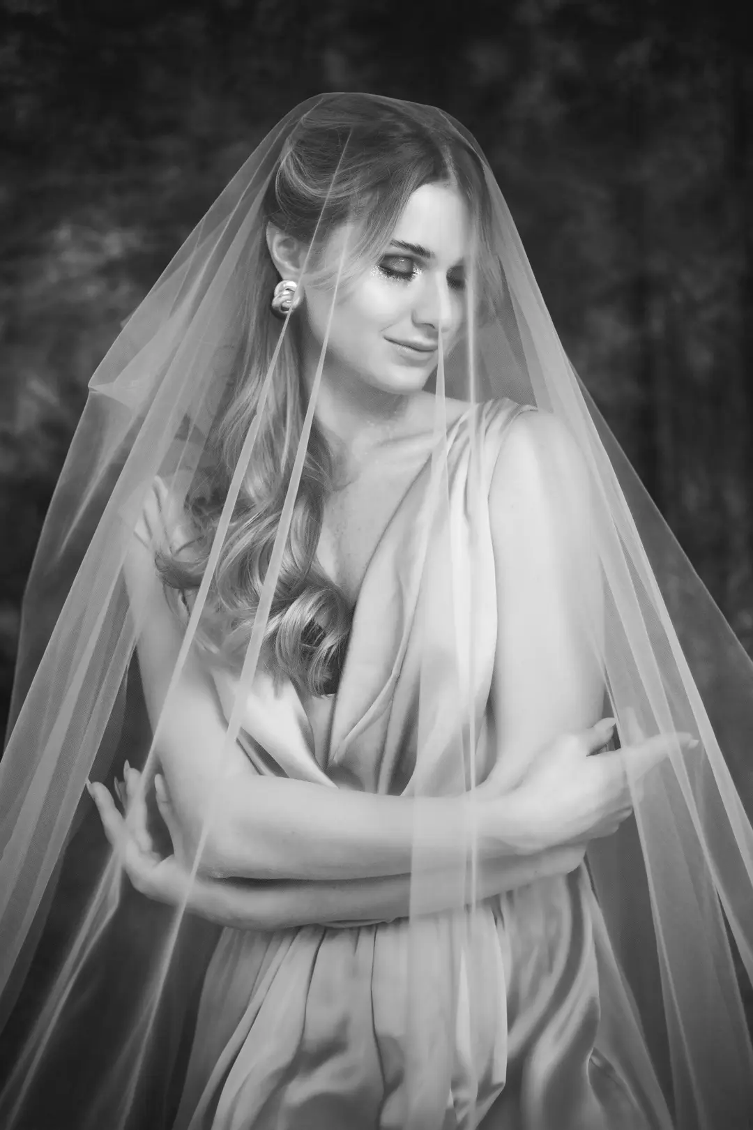 Black and white portrait of a woman under a sheer veil, eyes closed, arms crossed